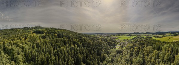 A sweeping view of dense forests and green fields in a quiet valley, lit up by the afternoon sun. Nature shows its beauty and diversity in this peaceful landscape. Perlbachtal, Neukirchen, Lower Bavaria