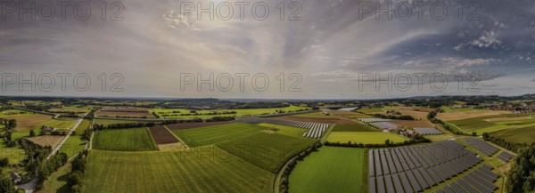 The panoramic view shows an expansive rural landscape in Germany, criss-crossed by fields and agricultural land, complemented by solar energy systems under a clear sky. Hunderdorf, Lower Bavaria