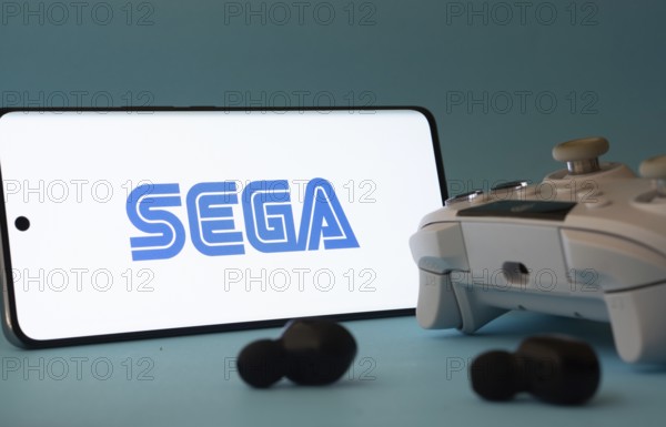 Dhaka, Bangladesh- 13 Sep 2025: A smartphone with the Sega icon next to a controller and earbuds on a blue surface