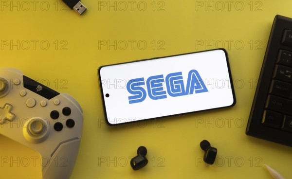 Dhaka, Bangladesh- 13 Sep 2025: Smartphone with Sega logo, game controller, and earbuds on a yellow background