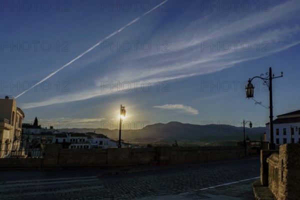 Sun rising behind mountains, illuminating street lamps on cobblestone bridge at dawn in ronda, spain in ronda, malaga, spain