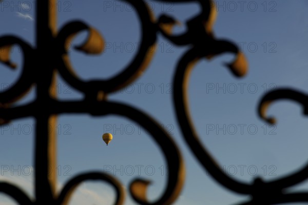 Yellow hot air balloon flying against a blue sky, seen through an ornate metal gate in ronda, malaga, spain