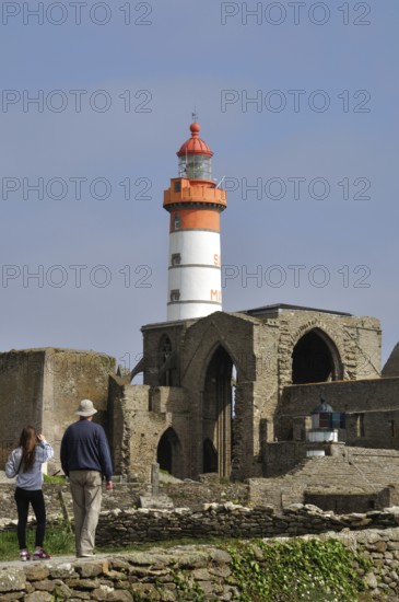 Pointe St Mathieu and Abbey Lighthouse, A historical lighthouse stands amidst ancient stone ruins under a clear blue sky, with people walking nearby in Brittany, France