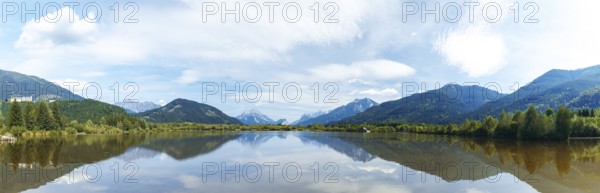 Panoramic lake reflects the surrounding mountains and the slightly cloudy sky, Admont, Styria, Austria