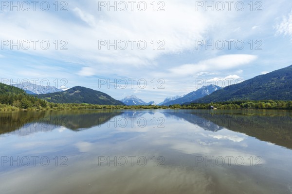 Panoramic lake reflects the surrounding mountains and the slightly cloudy sky, Admont, Styria, Austria