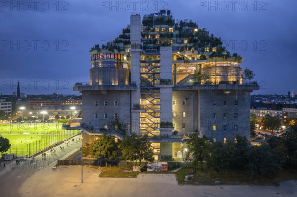 Aerial view of the Hamburg bunker on Heiligengeistfeld during the blue hour with illuminated floors and green trees at night, Hamburg, Germany