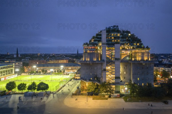 Aerial view of the Hamburg bunker on Heiligengeistfeld during the blue hour with illuminated floors and green trees at night, Hamburg, Germany