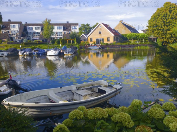 Boats on a quiet canal with reflection of houses in the water, surrounded by green landscape, Alblasserdam, Rotterdam, South Holland, Netherlands