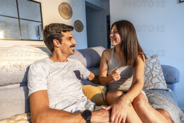 Young couple enjoying a relaxing afternoon together, sharing stories and laughter on their comfortable sofa in the natural light of their modern apartment