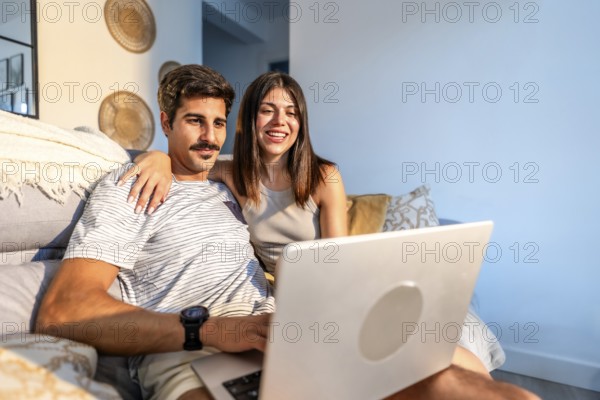 Young couple enjoying a streaming movie on a laptop, relaxing together on a comfortable sofa in their modern living room