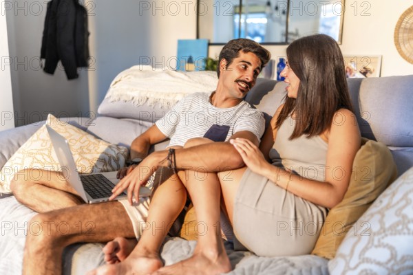 Young couple relaxing together on a comfortable sofa at home, browsing internet on a laptop and enjoying time together