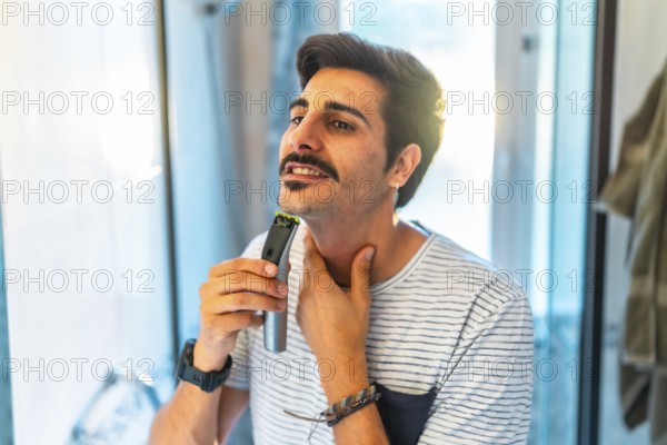 Man trimming his beard using an electric razor, taking care of his appearance in the bathroom mirror