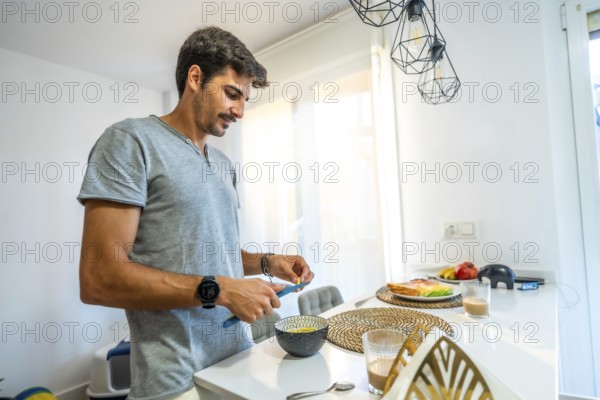 Young man spreading butter on fresh bread while enjoying breakfast in a bright, modern kitchen filled with natural light and comfort