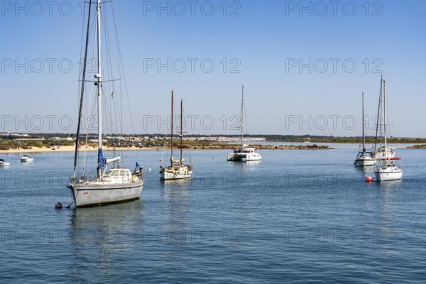 Sailboats anchored in the Gilão River, in front of the beach Praia da Ilha de Tavira, on the island off Tavira, Algarve, Portugal