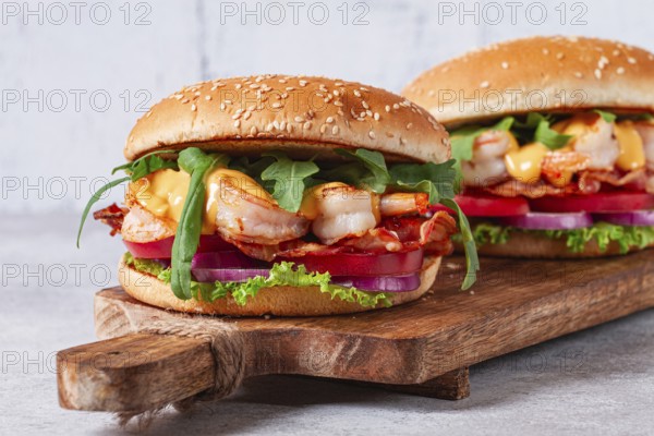 Two shrimp burgers and buns with sesame seeds, bacon, lettuce, tomatoes and onions, On a wooden board