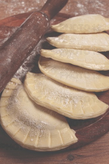 Raw chebureks, mini, on a cutting board, wooden table, close-up, no people