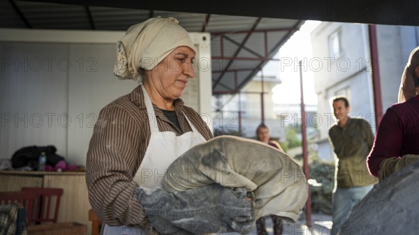 A Turkish woman bakes traditional bread on a clay tandoor oven in a rural village, Hatay, Hatay, Türkiye