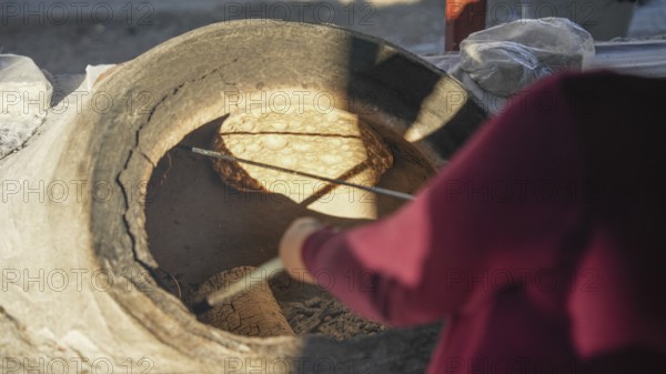 A Turkish woman bakes traditional bread on a clay tandoor oven in a rural village, Hatay, Hatay, Türkiye