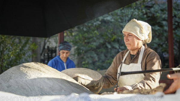 A Turkish woman bakes traditional bread on a clay tandoor oven in a rural village, Hatay, Hatay, Türkiye