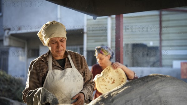 A Turkish woman bakes traditional bread on a clay tandoor oven in a rural village, Hatay, Hatay, Türkiye