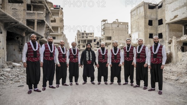 A Syrian traditional Arada troupe pose in traditional attire amid destroyed buildings in a war-torn neighborhood of Damascus. The folkloric performance, part of celebrations, remains a symbol of Syrian cultural identity, Damascus, Damascus, Syria