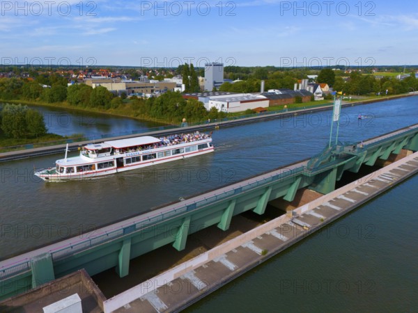 A passenger ship sails on a canal over a large bridge, surrounded by city buildings and nature, waterway crossing, Mittellandkanal over Weser, trough bridge, Minden, North Rhine-Westphalia, Germany