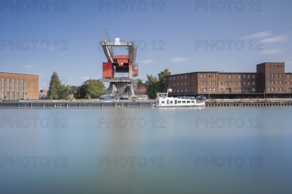 View over the Mittelland Canal to an industrial building and a crane in front of a ship, long exposure, Garbsen, Hanover, Lower Saxony, Germany
