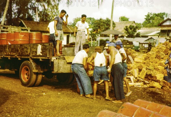 Male workers loading metal fuel drums onto back of lorry in timber yard, Johor Bahru, Johor, Malaya, Malaysia, south east Asia 1963
