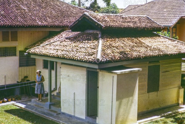 British expatriate woman standing outside next to quarters of her Amha domestic servant, 3 Jalan View, Johor Bahru, Malaya, Malaysia, south east Asia 1963