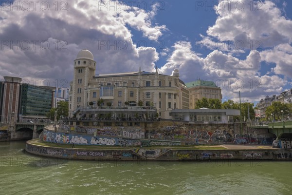 A historic building by the river with graffiti, under a clear sky, surrounded by urban surroundings Urania Ringstrasse Vienna Austria