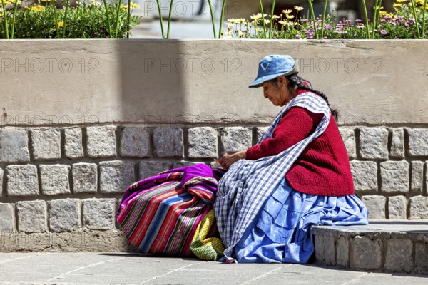 Woman in traditional dress sitting next to a stone wall and resting, Traditionally dressed woman in the streets of La Paz Bolivia