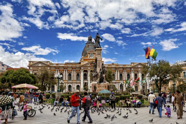 Lively square with pigeons and people in front of a historic building and a statue under a blue sky, The Presidential Palace of La Paz in Bolivia