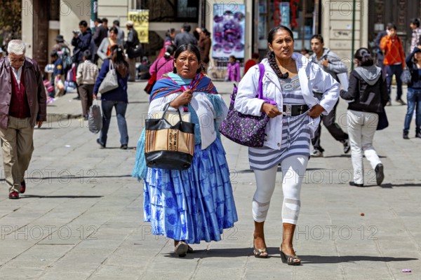 Two woman in traditional and modern dress walk on a busy street, Traditionally dressed woman in the streets of La Paz Bolivia