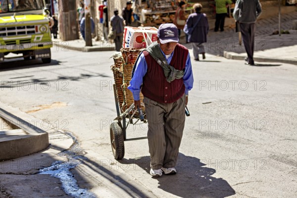 An elderly man pulls a handcart through a sunny city street, A man pulls a handcart through the streets of La Paz in Bolivia