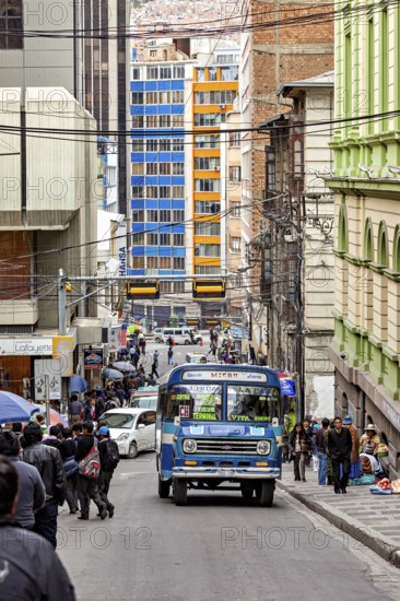 Busy city street with a blue bus and many people during the day in the middle of tall buildings, A colourful bus drives through the streets of La Paz in Bolivia
