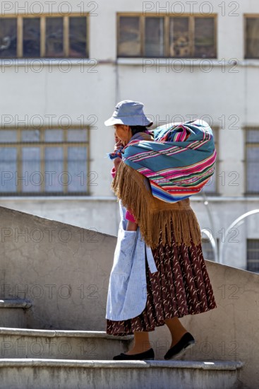 A woman carries a colourful bag and climbs a staircase in front of a building view, Traditionally dressed woman in the streets of La Paz Bolivia