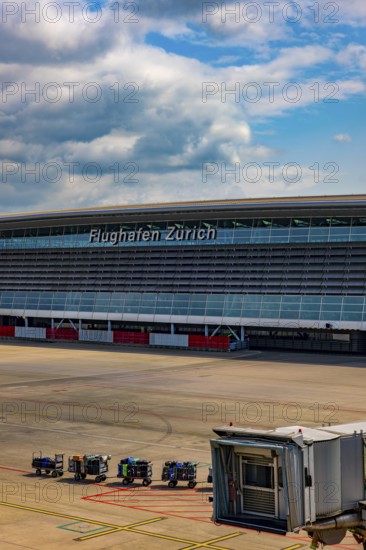 Zurich Airport and Building and Boarding Bridge Gate and Lugage on Trailer on Airfield in a Sunny Summer Day From the Airport in Kloten, Zurich, Zurich Canton, Switzerland