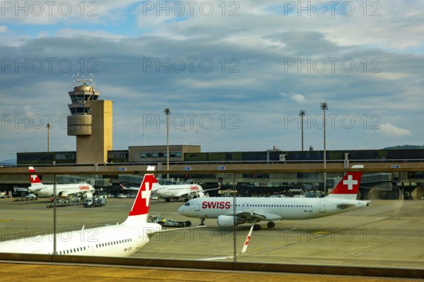 Swiss Airlines Passenger Airplane and Air Traffic Control Tower on the Airfield in a Sunny Summer Day with Blue Sky and Clouds From the Airport in Kloten, Zurich, Zurich Canton, Switzerland