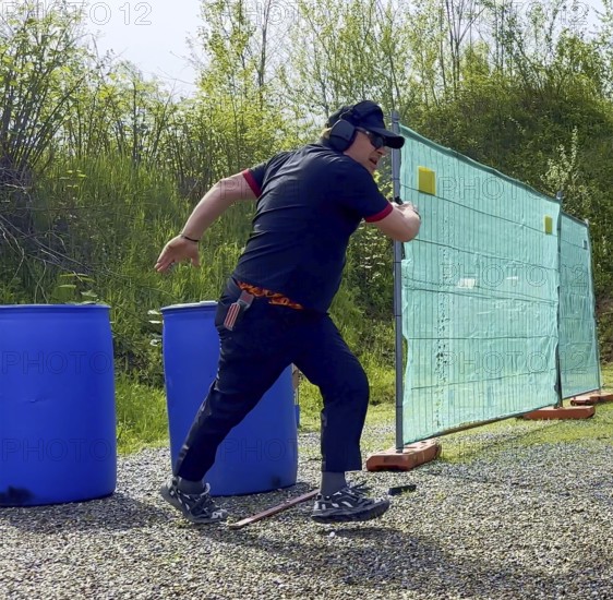 Man with Cap and Protection Eyeglasses Running and Holding a Handgun Backward in IPSC Shooting Sport in Switzerland