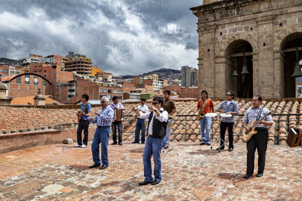 Group of musicians on a tiled roof in front of an urban backdrop with clouds in the sky, A music group above the rooftops of La Paz in Bolivia