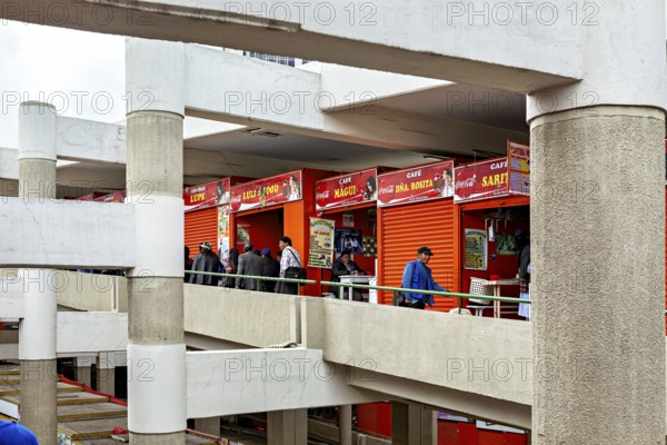 People walk through the upper floors of a modern market with red facades, Small shops and restaurants in the market halls of La Paz in Bolivia