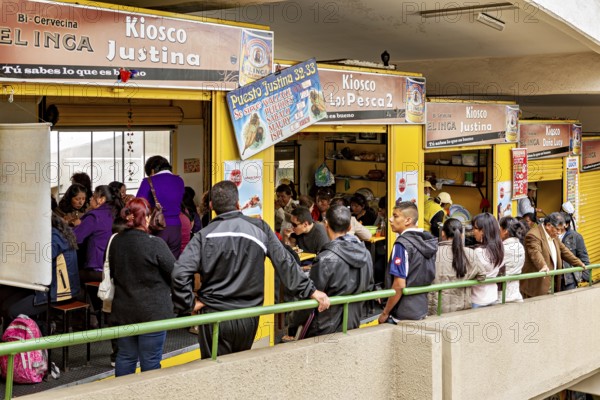 Lots of people gather at yellow market stalls, lively shopping atmosphere, small shops and restaurants in the market halls of La Paz in Bolivia