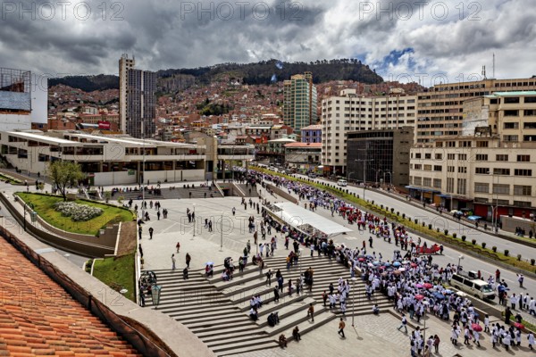 Overview of busy urban environment with crowds, modern buildings and a mountain backdrop, A demonstration in the streets of La Paz, Bolivia