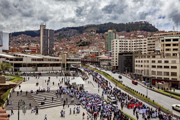 Bustling city atmosphere with people gathering in a large square surrounded by urban architecture and mountains, A demonstration in the streets of La Paz, Bolivia