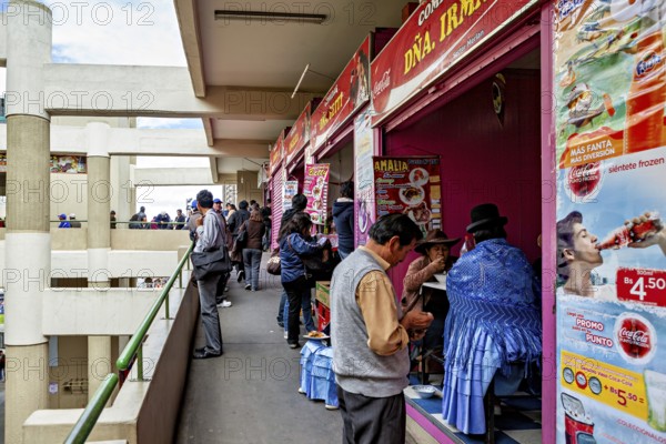 Market goers in lively surroundings at food stalls, some wearing traditional clothing, Small shops and restaurants in the market halls of La Paz in Bolivia