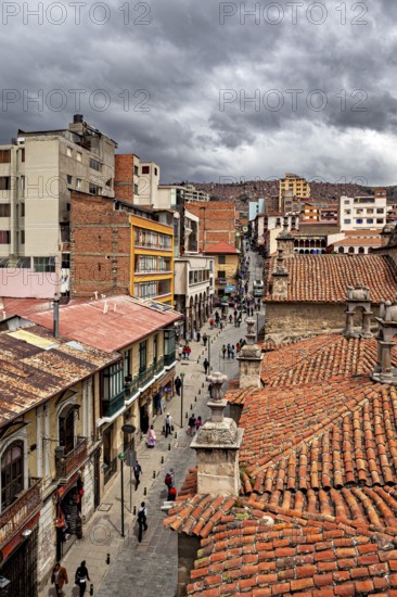 Historic city view with red tiled roofs under a cloudy sky, people in the streets of La Paz in Bolivia