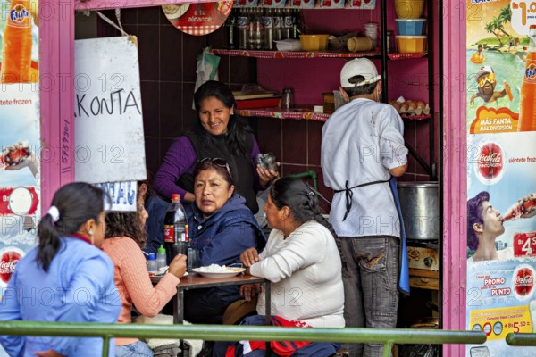 People enjoy their meals in the middle of a lively street snack bar, surrounded by colourful posters, small shops and restaurants in the market halls of La Paz in Bolivia