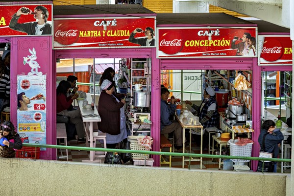 Friendly café with people eating, eye-catching Coca-Cola advert, Small shops and restaurants in the market halls of La Paz in Bolivia