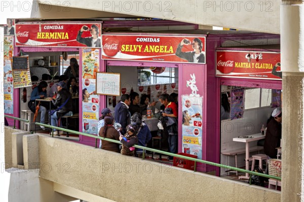 Lively food stalls with smiling people and Coca-Cola adverts, convivial atmosphere, small shops and restaurants in the market halls of La Paz in Bolivia