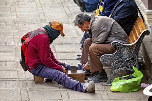 A shoeshine boy works on a pavement polishing the shoes of a seated man, shoeshine boy in the streets of La Paz, Bolivia